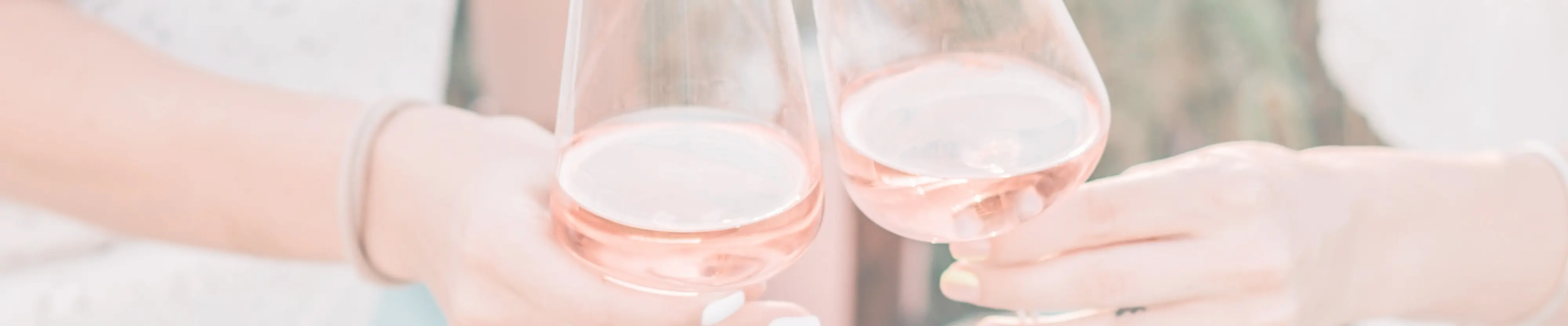 2 Gläser sind mit Rosé Wein gefüllt und in der Mitte wird angestossen.