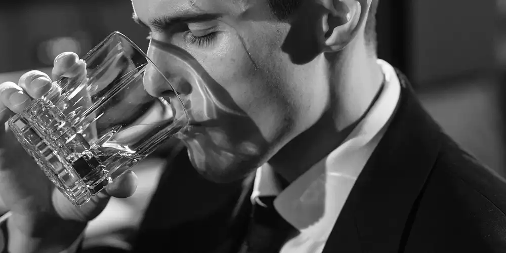 Schwarz-Weiss-Bild von einem Herren, der Whiskey trinkt.